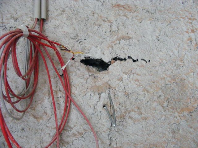 Zonă de beton cu o fisură mică deschisă și cabluri electrice roșii